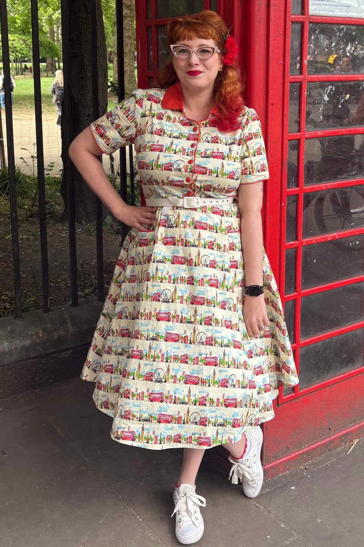 Woman in a vintage-style London print dress standing next to a red telephone box.
