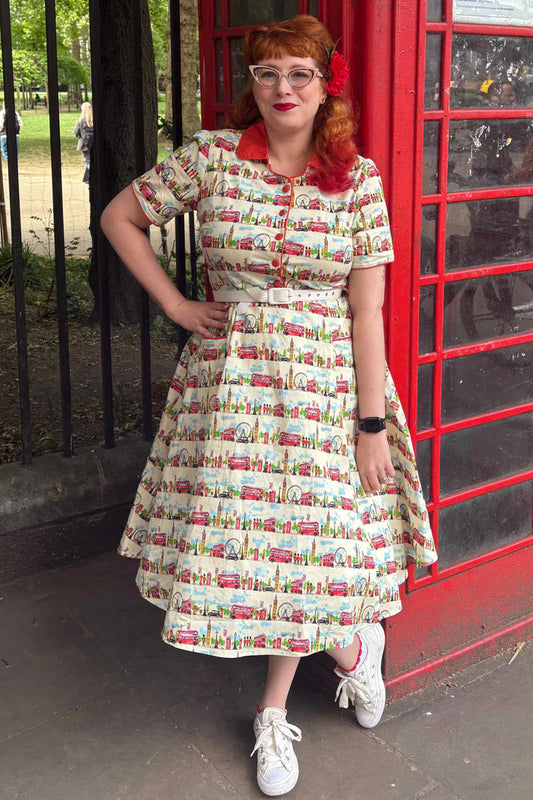 Woman in a vintage-style London print dress standing next to a red telephone box.