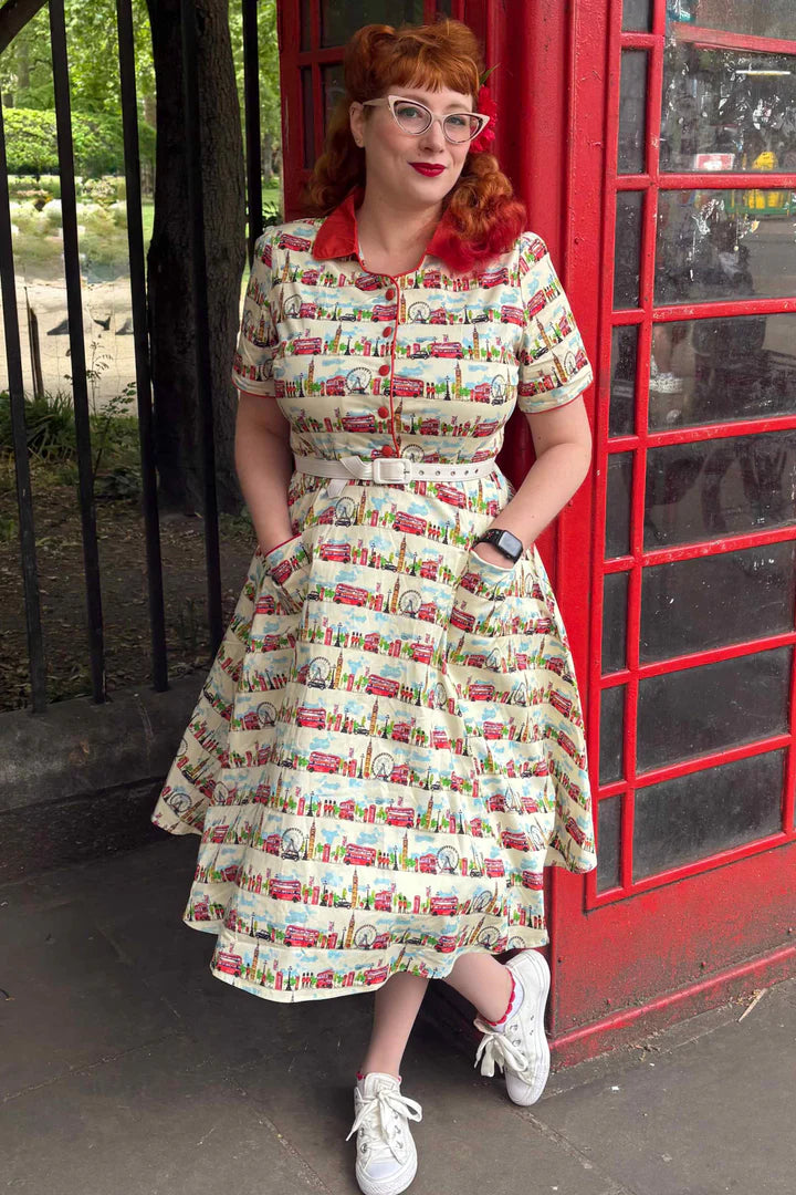 Woman in a vintage-style dress with retro London pattern standing next to a red phone booth.